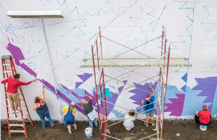 A group of people painting a blue and purple mural on a white wall.
