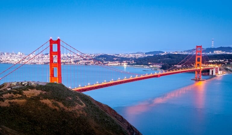 This image shows the Golden Gate Bridge in the foreground and the city of San Francisco lit up at night in the background.