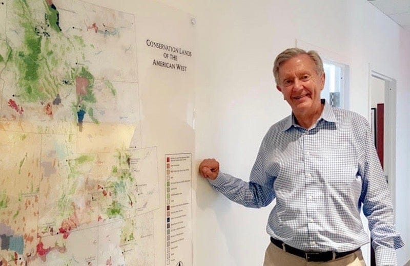 A man in a dress shirt stants to the side of a map showing the topography and geography of the Western United States.