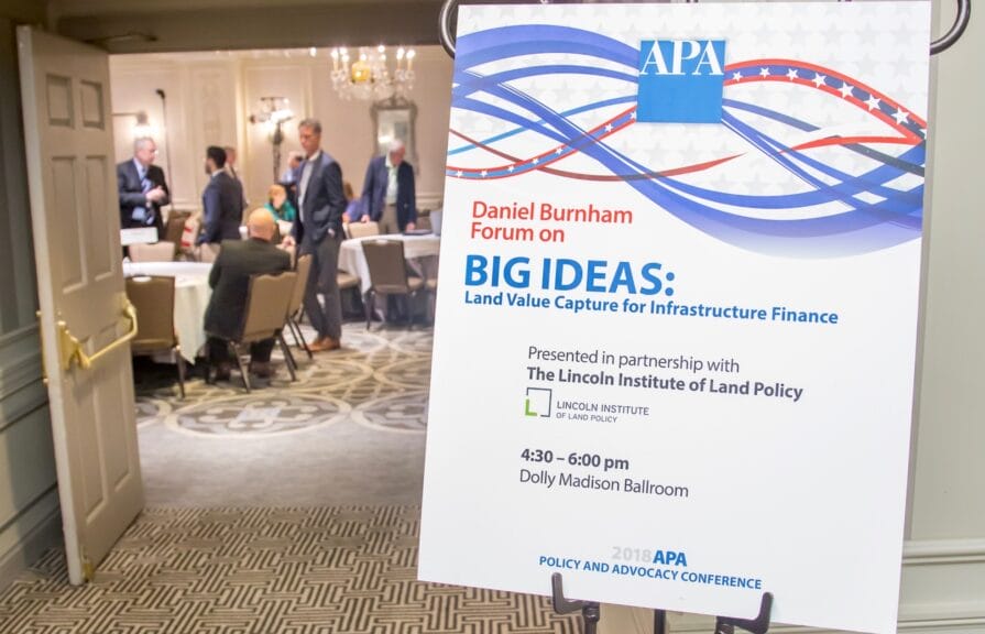 A placard occupies the right side of the frame. It reads Daniel Burnham Forum on Big Ideas: Land Value Capture for Infrastructure Finance. On the left side