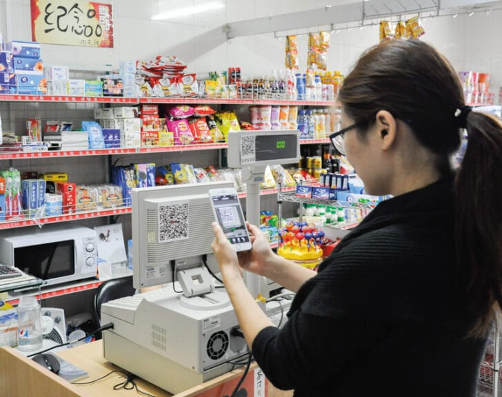 A woman scans a QR code that is taped to a cash register in a grocery store in Beijing
