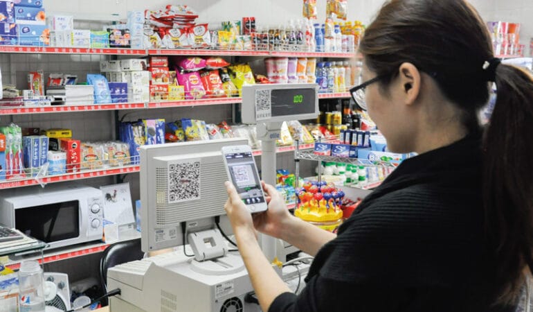 A woman scans a QR code that is taped to a cash register in a grocery store in Beijing