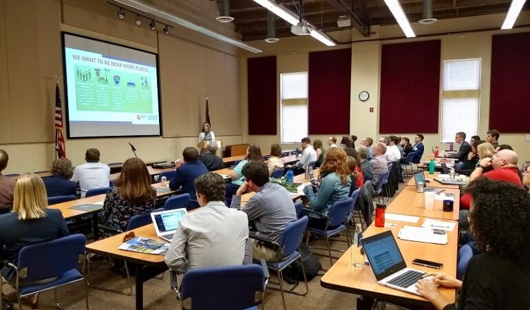 40 conference participants sit at desks looking at a power point presentation during the second annual Consortium for Scenario Planning Conference.