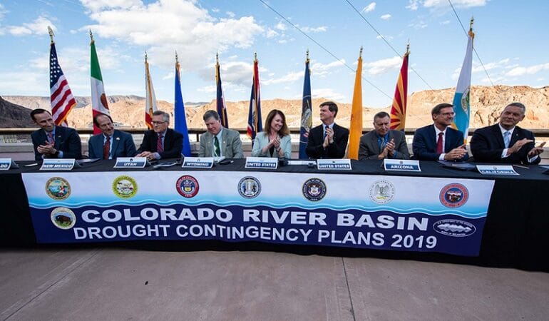 Federal and state officials sit at a table to celebrate the signing of the Colorado River drought contingency plan atop the Hoover Dam