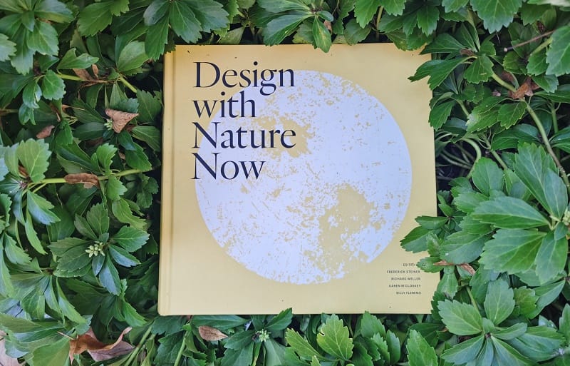 An image of the book Design with Nature Now surrounded by leaves.