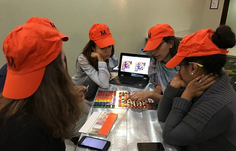 Un grupo de participantes en un curso del Instituto Lincoln usa sombreros naranjas y se reúne alrededor de un tablero de juego.