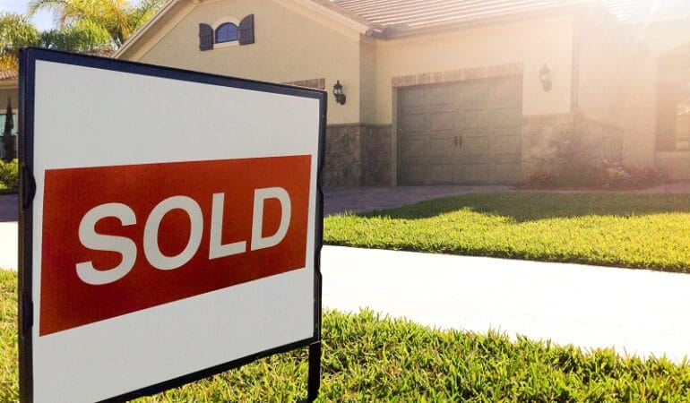 A "sold" sign sits on a front lawn in front of a large home.