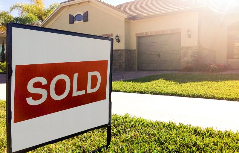 A "sold" sign sits on a front lawn in front of a large home.