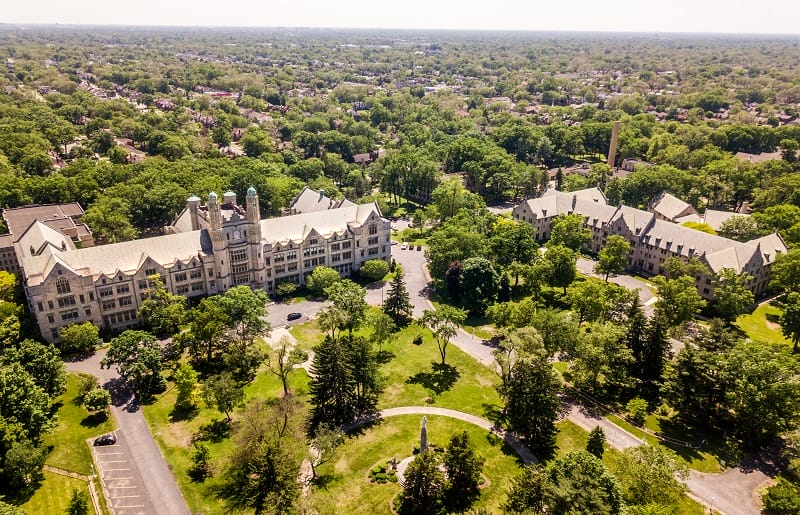 An aerial view of the Marygrove College campus and surrounding neighborhood. The campus and neighborhood have many trees. The two most visible buildings on the campus are old
