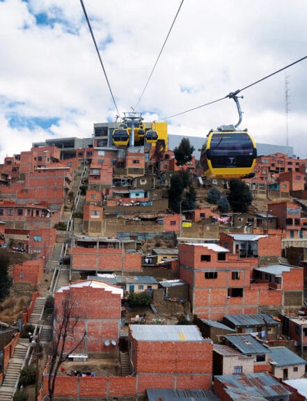 Teleféricos aéreos amarillos viajan por una colina en América Latina sobre asentamientos informales hechos de ladrillos. Crédito: Gwen Kash