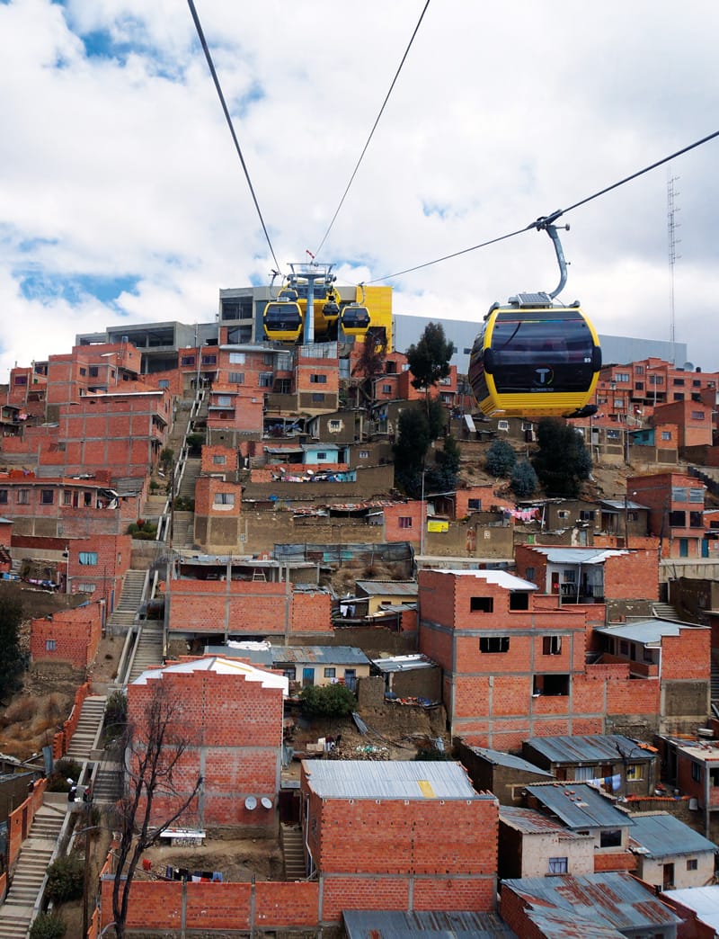 Teleféricos aéreos amarillos viajan por una colina en América Latina sobre asentamientos informales hechos de ladrillos. Crédito: Gwen Kash