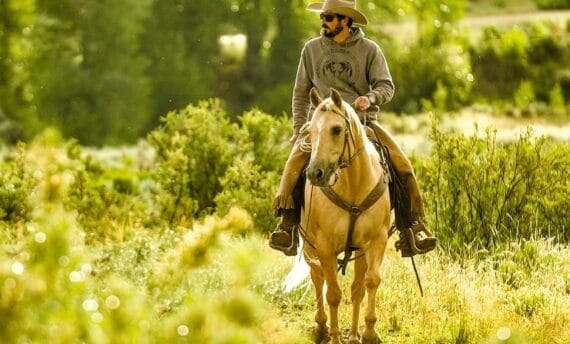 Colorado rancher Paul Bruchez rides a horse in a green field.