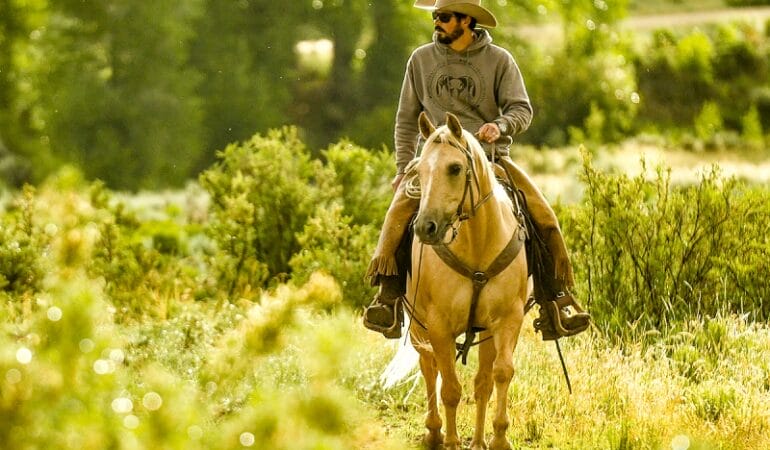 Colorado rancher Paul Bruchez rides a horse in a green field.