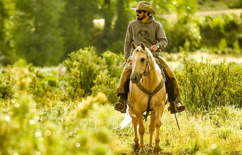 Colorado rancher Paul Bruchez rides a horse in a green field.