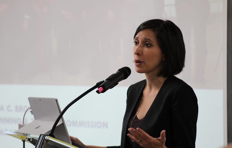 Sara Bronin speaks into a microphone. The background shows her power point presentation.