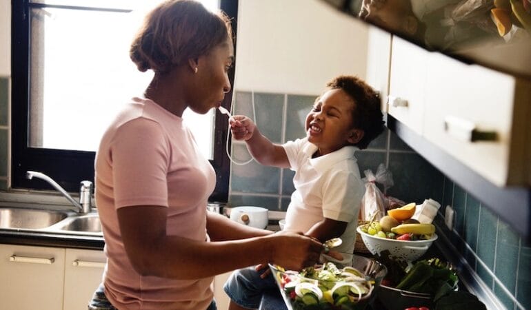 A woman feeds a toddler in a kitchen.