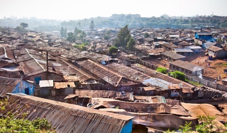 Shacks with corregated metal roofs are crowded together in most of the foreground