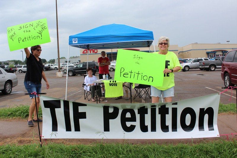 People hold neon green signs behind a large white banner reading TIF Petition in black letters.