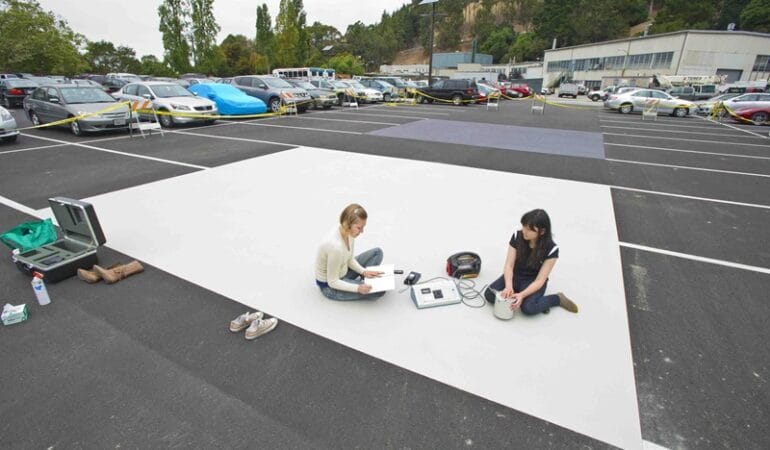 Two people sit on a square of white paint in a paved parking lot