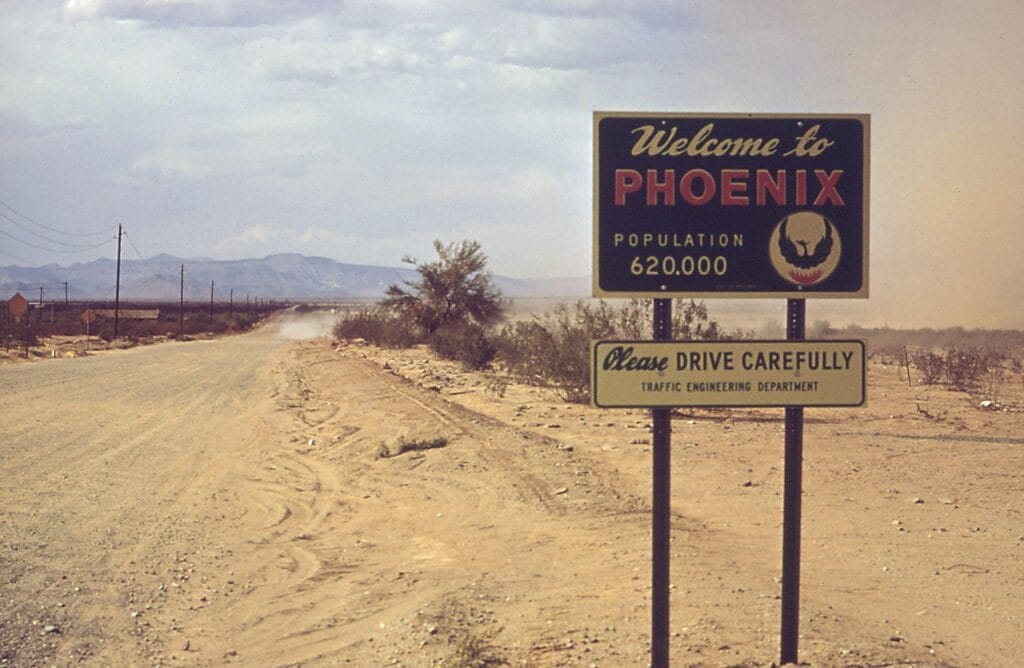 A sign reading 'welcome to Phoenix' in front of an unpopulated desert and distant mountains.