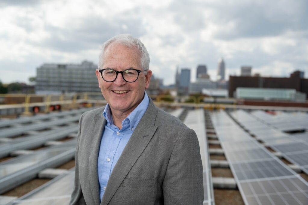 Portrait of Mike Foley on a rooftop with solar panels and downtown Cleveland in the background.