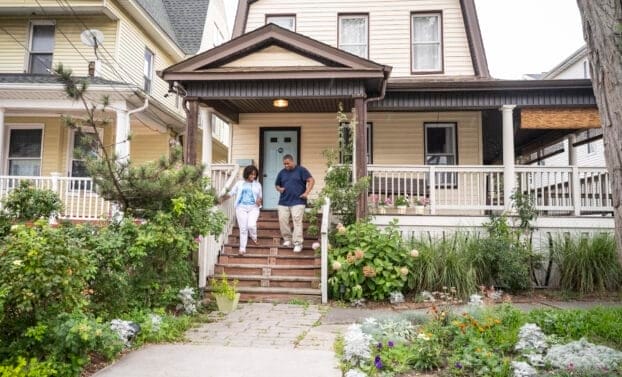 Full length view of casually dressed Black man and woman, smiling as they leave home on summer day in Rockaway Beach, Queens.