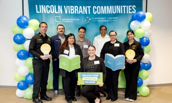 Members of the Lincoln Vibrant Communities Teams cohort, posing in front of a blue banner with the title Lincoln Vibrant Communities. The banner is surrounded by white, blue and light green colored balloons.