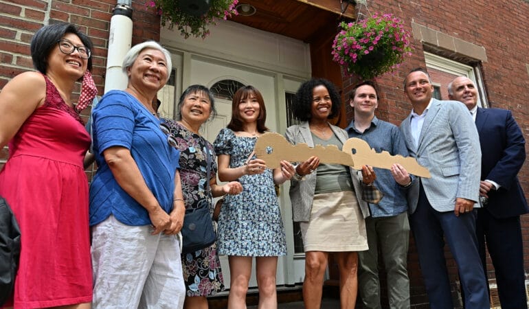 A group of 8 people holding cardboard keys on a porch of a house