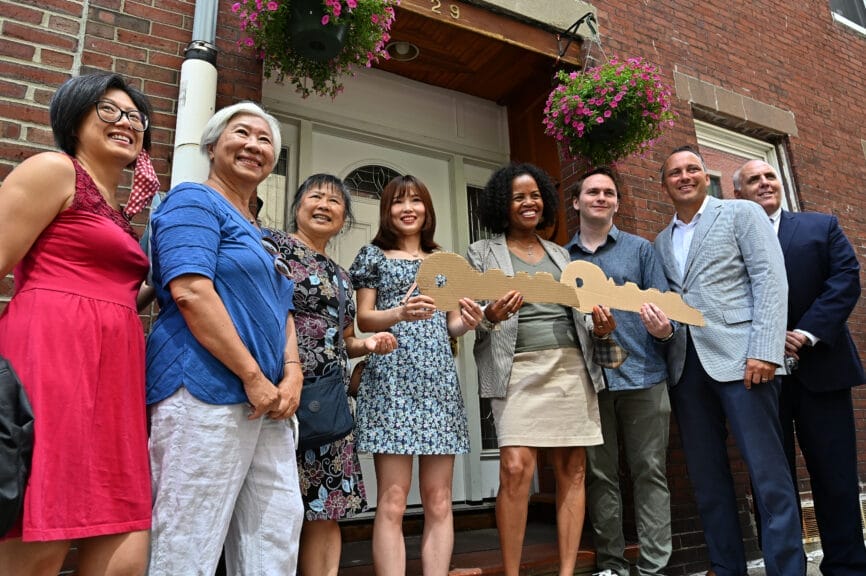 A group of 8 people holding cardboard keys on a porch of a house