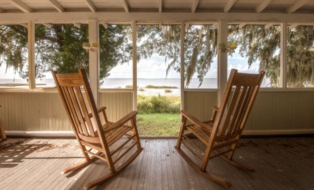 Looking out from a porch toward water on Sapelo Island, Georgia. Two empty rocking chairs are in the foreground, facing away from the camera toward the water.