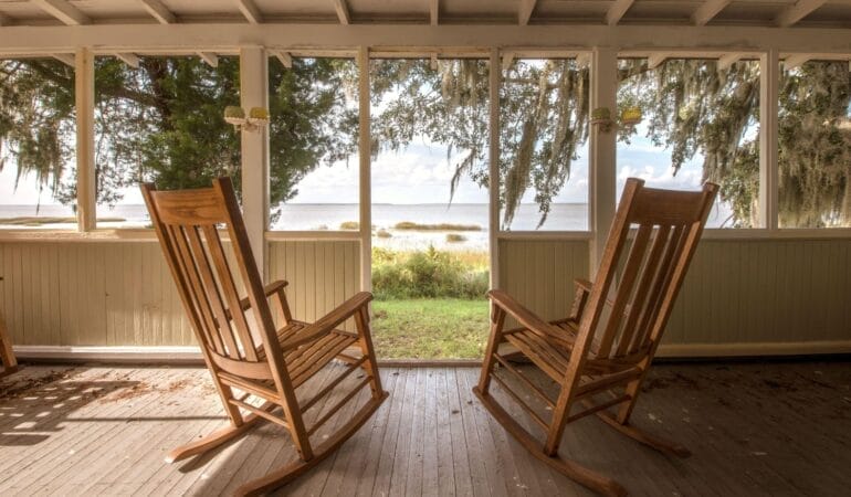 Looking out from a porch toward water on Sapelo Island, Georgia. Two empty rocking chairs are in the foreground, facing away from the camera toward the water.