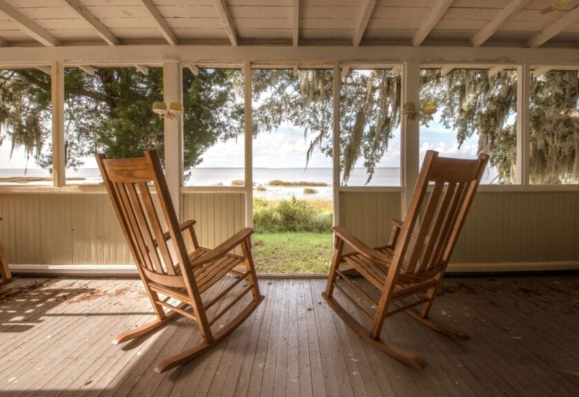 Looking out from a porch toward water on Sapelo Island, Georgia. Two empty rocking chairs are in the foreground, facing away from the camera toward the water.