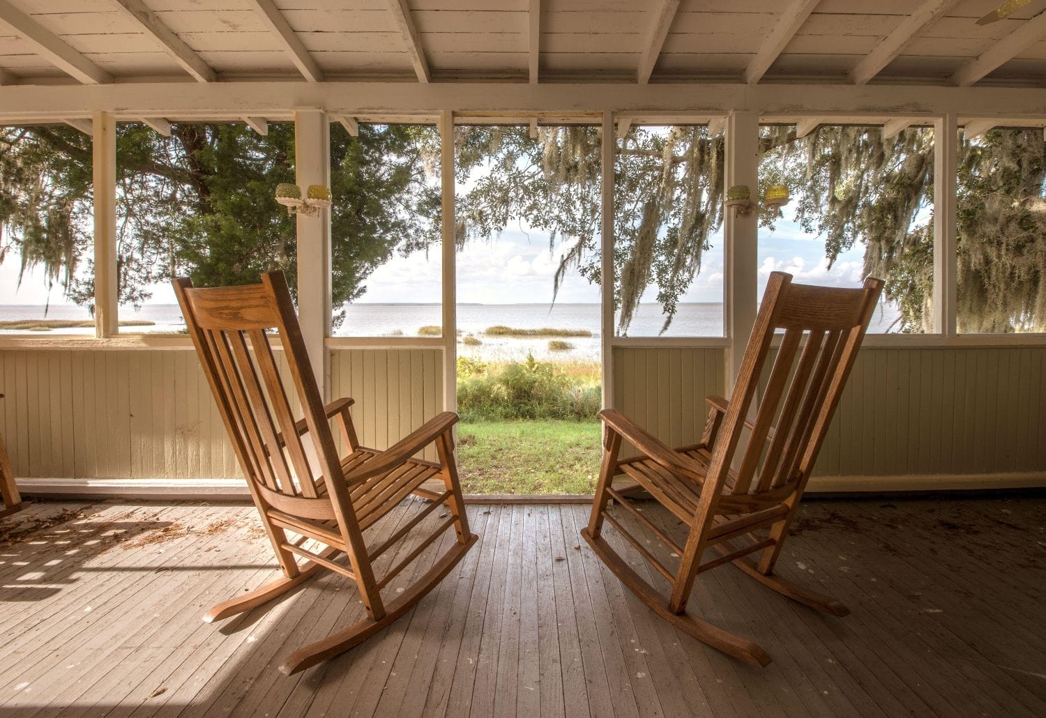 Looking out from a porch toward water on Sapelo Island, Georgia. Two empty rocking chairs are in the foreground, facing away from the camera toward the water.