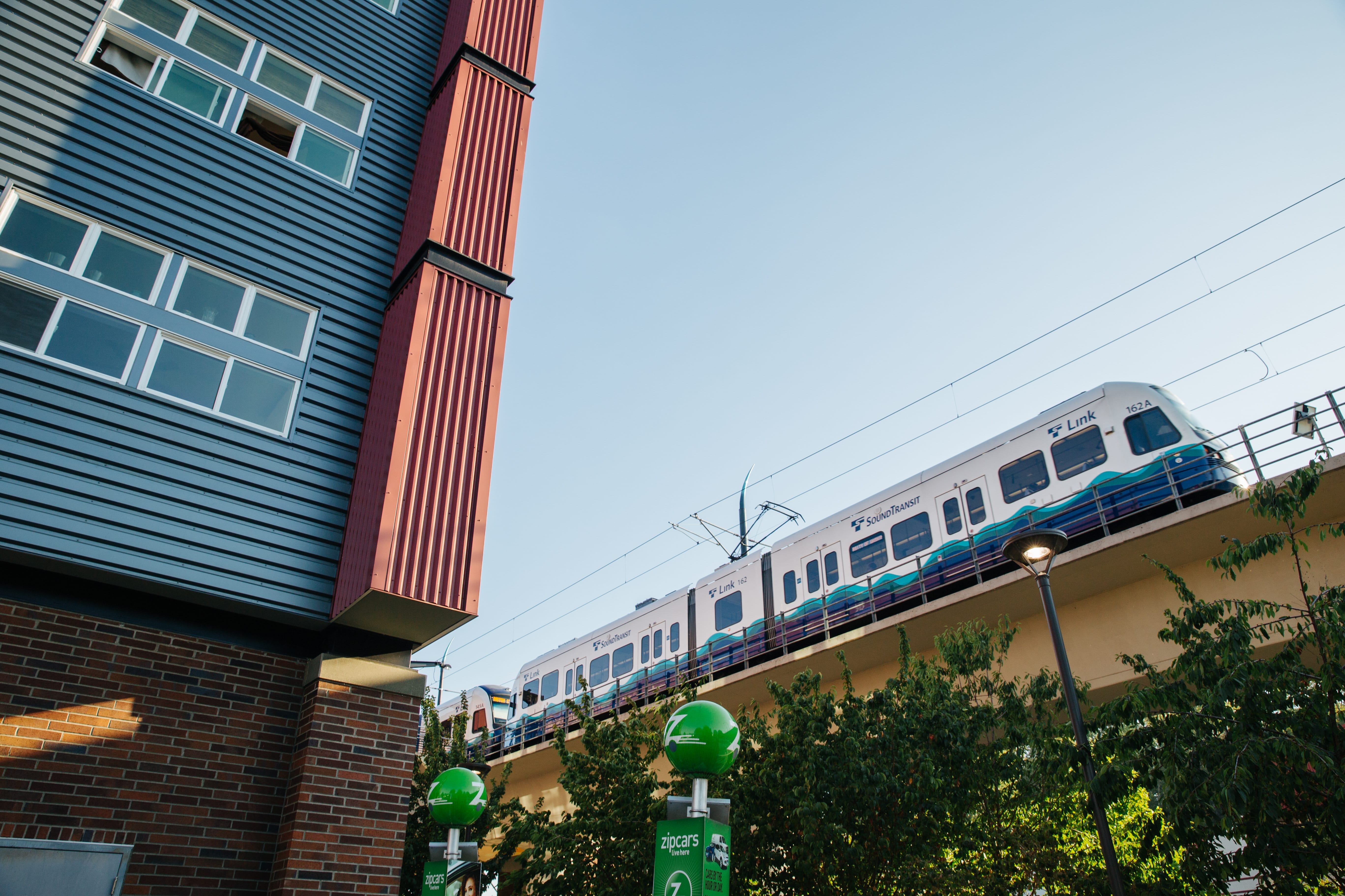 Elevated mass transit train in background with an apartment building in foreground.