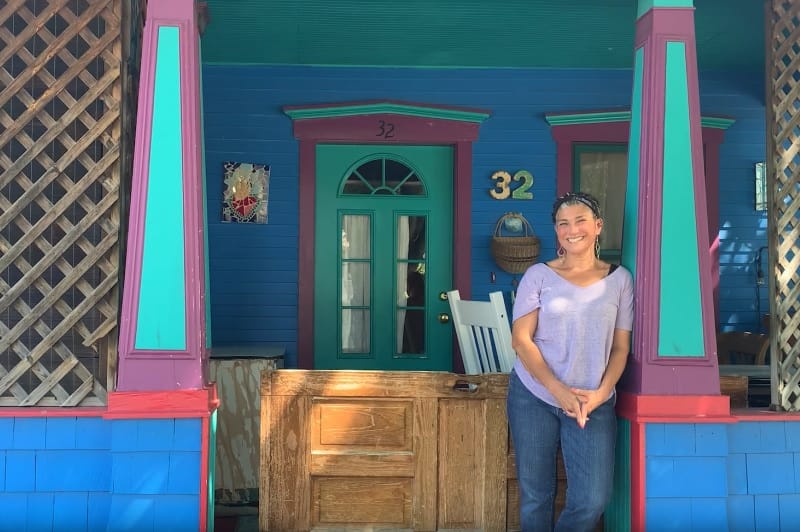 A woman smiling in the doorway of a blue house