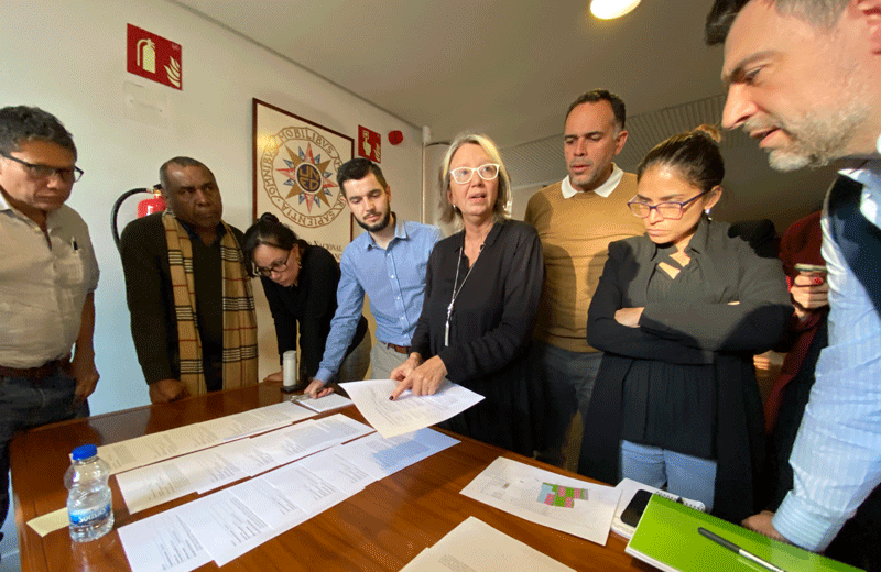 Students stand around a table, collaborating during a interactive session during the course in Madrid.